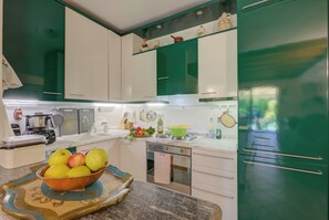 Een keuken met witte en groene kastjes, een schaal fruit op het aanrecht en een groene koelkast.
