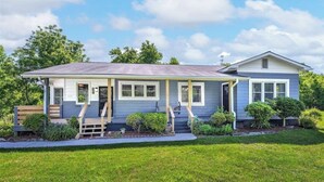 A single-story house with a porch, a front yard, and a clear blue sky. - Spacious Family Retreat  2 Indoor Fireplaces + Volleyball Fun! (Flat Rock)