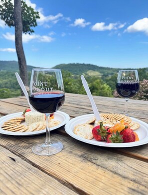 Due tavoli da picnic con bicchieri di vino e piatti di snack, con le montagne sullo sfondo.