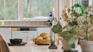 Uma cozinha com janela, uma vela, um copo, uma cesta de pão e um vaso de planta.