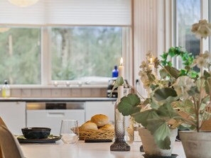 Una cocina con ventana, una vela, un vaso, una cesta de pan y una planta en maceta.