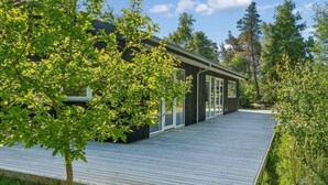 Uma casa moderna com deck de madeira, grandes janelas e cercada por árvores.
