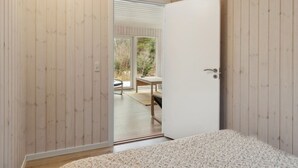 Quarto com paredes de madeira, porta branca e vista para um pátio externo com mesa e cadeiras.