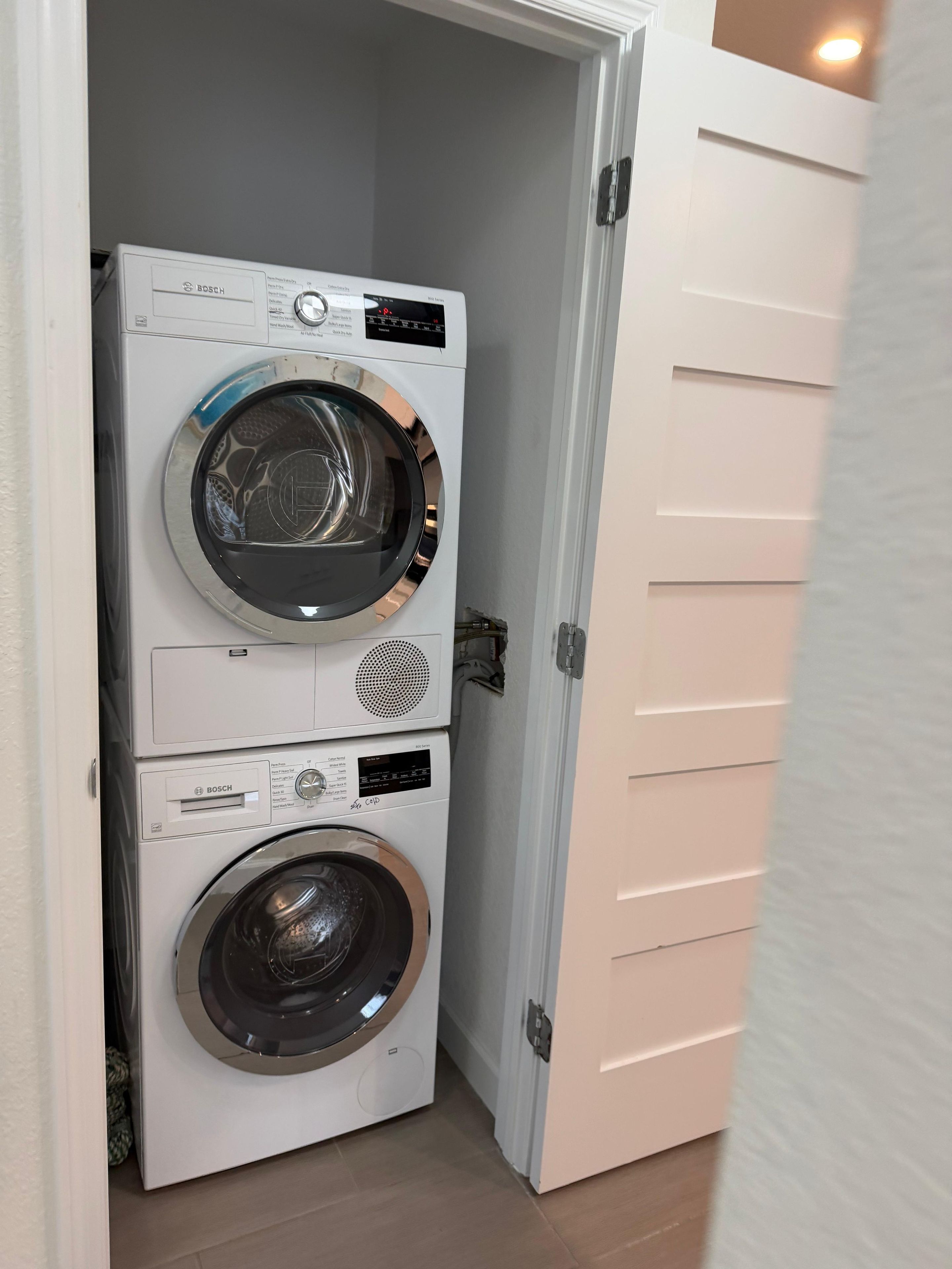 Un lavadero pequeño y blanco, de dos puertas, con lavadora y secadora Bosch.