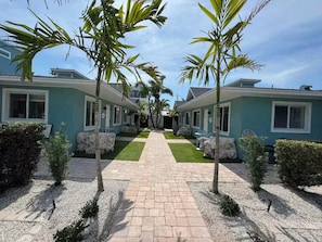 A pathway leading to a row of two-story buildings with a central lawn. - "St.Thomas" Villa: 2 Min Walk to Beach : Beach Gear: Tranquil Courtyard: 2BR/2BA (Bradenton Beach)