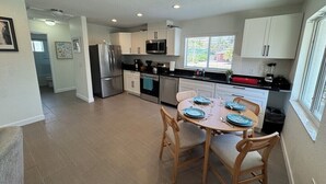A modern kitchen with white cabinets, stainless steel appliances, and a dining area with a round table set for four. - "St.Thomas"-Family Villa-2 Blks 2 Beach-BeachGear-2 BR 2 BA-Tranquil Courtyard (Bradenton Beach)