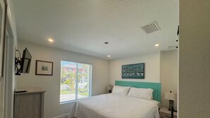 A bedroom with a bed, a nightstand, a window with blinds, a painting on the wall, and a ceiling vent. - "St.Thomas"-Family Villa-2 Blks 2 Beach-BeachGear-2 BR 2 BA-Tranquil Courtyard (Bradenton Beach)
