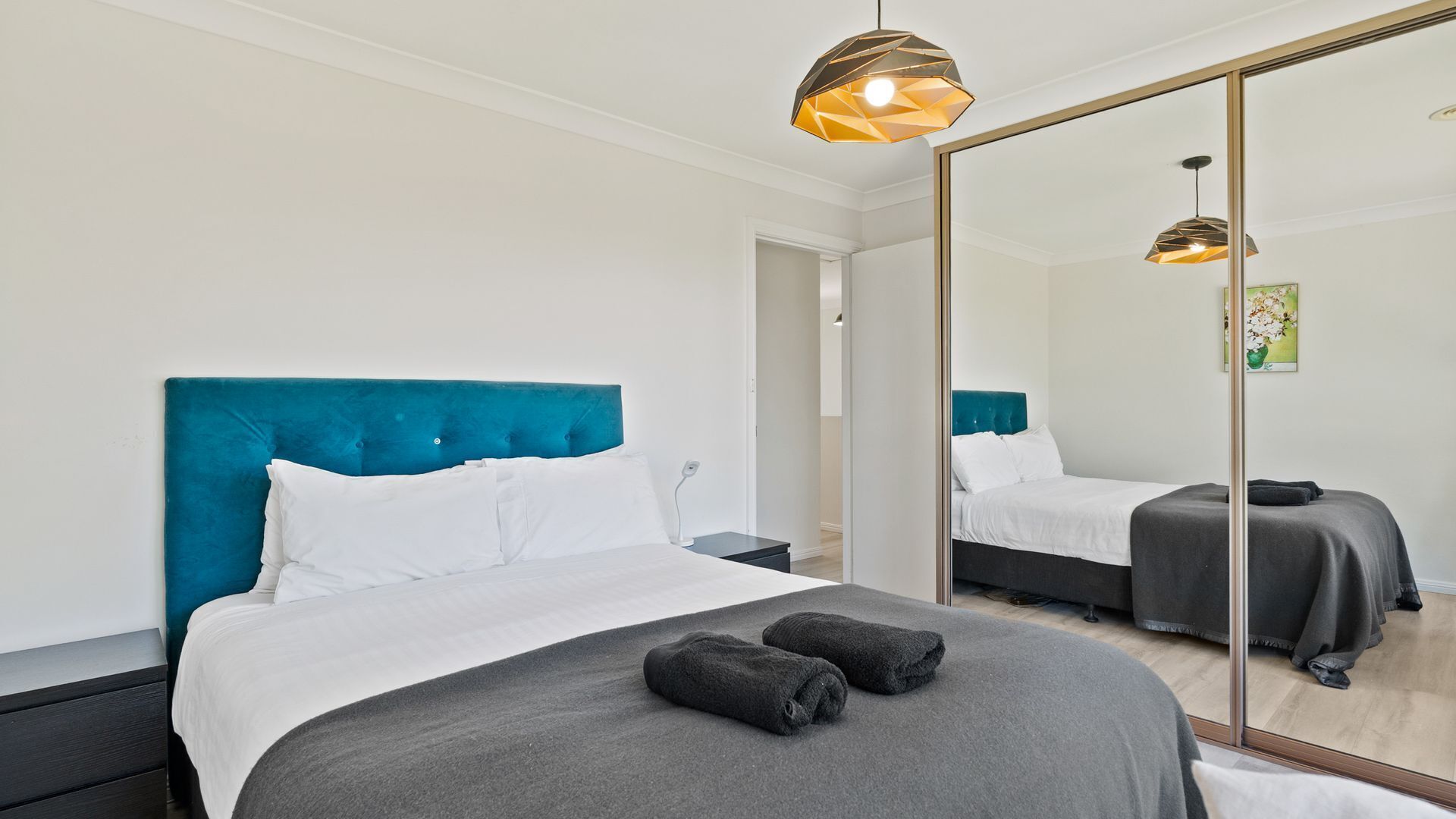 A modern hotel room with a large mirror, a blue headboard, and two neatly folded towels on the bed.