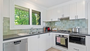 A modern kitchen with white cabinets, stainless steel appliances, a Bosch dishwasher, and a window with blinds. - Fern & Maple Lodge Wentworth Falls (Wentworth Falls)