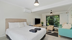 A modern hotel room with a large bed, a flat-screen TV, a sofa, and a view of greenery through the windows. - Fern & Maple Lodge Wentworth Falls (Wentworth Falls)
