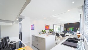 A modern kitchen with a central island, a dining area with a TV, and a living space with a large window. - Modern Villa 3BR - Great Location KL3 (Hua Hin)