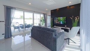 A modern living room with a grey sofa, a white armchair, a flat-screen TV, and a dining area with a table and chairs. - Modern Villa 3BR - Great Location KL3 (Hua Hin)