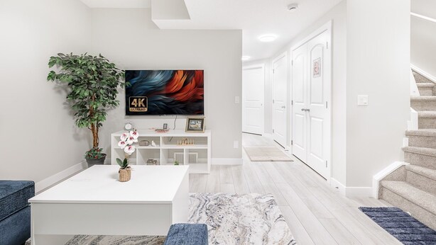 A modern living room with a flat-screen TV, a coffee table, a potted plant, and a staircase. - Charming 2Bed Retreat near Airport & Banff w/ desk (Airdrie)