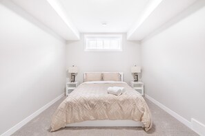A bedroom with a bed centered under a skylight, flanked by nightstands with lamps. - Charming 2Bed Retreat near Airport & Banff w/ desk (Airdrie)