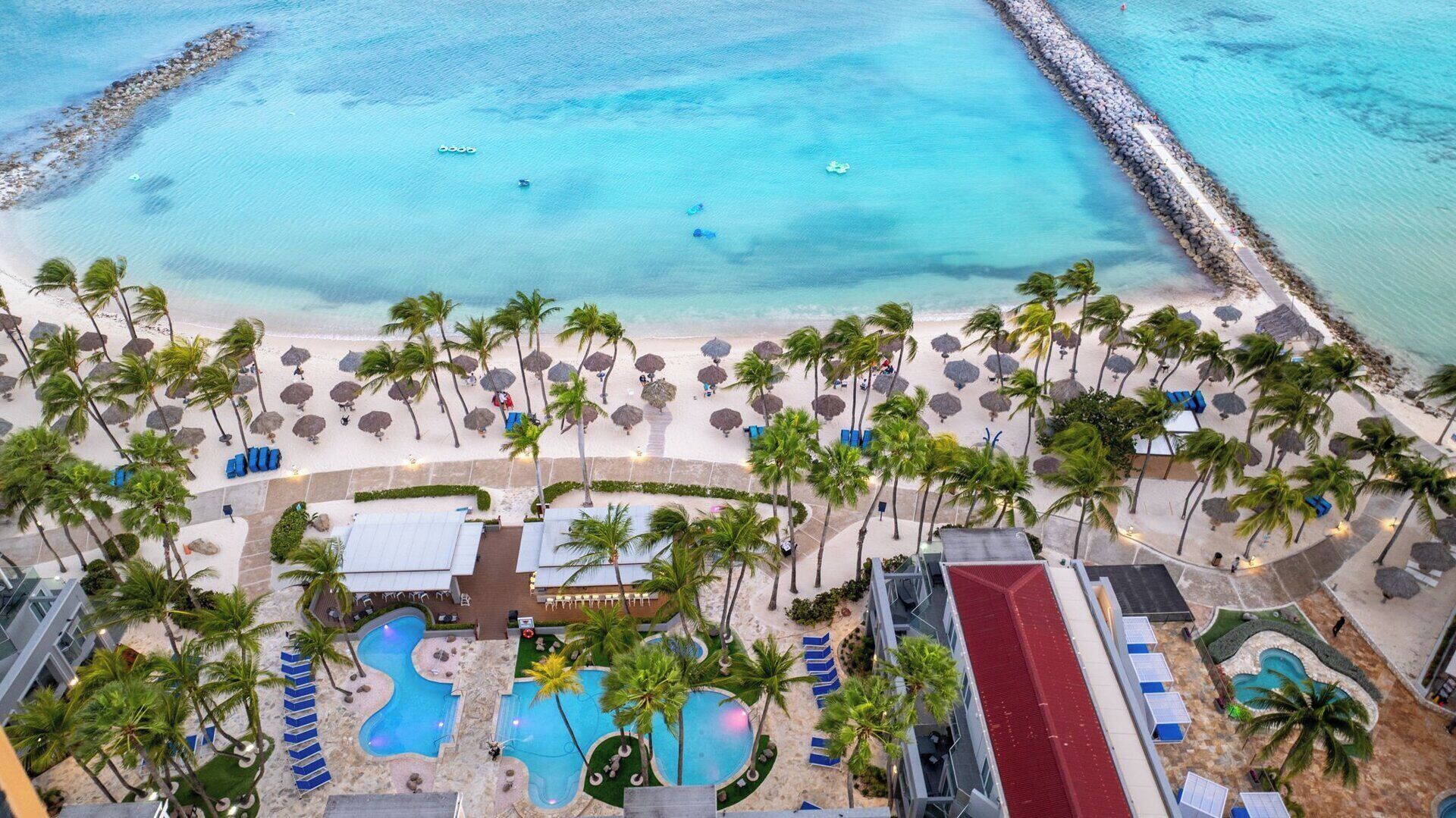 Vista aérea de um resort com praia, palmeiras e área de piscina.