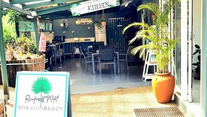 A reception area with a sign for Rainforest Motel Mission Beach, outdoor seating, and potted plants. - Rainforest Motel (Mission Beach)