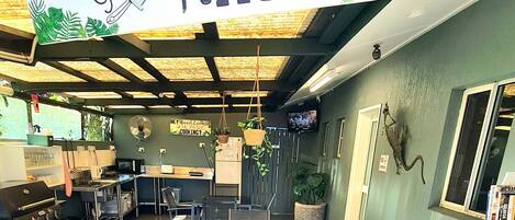 Et tekøkken med et skilt der står "Rainforest Motel's Guest Kitchen", med et rustikt loft, en kaffemaskine, en vask og en reol med bøger.