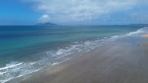 A beach with clear water and a distant mountain. - Rainforest Motel (Mission Beach)