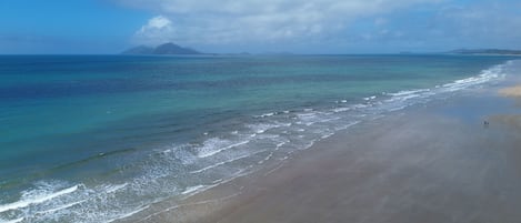 Een strand met helder water en een berg in de verte.