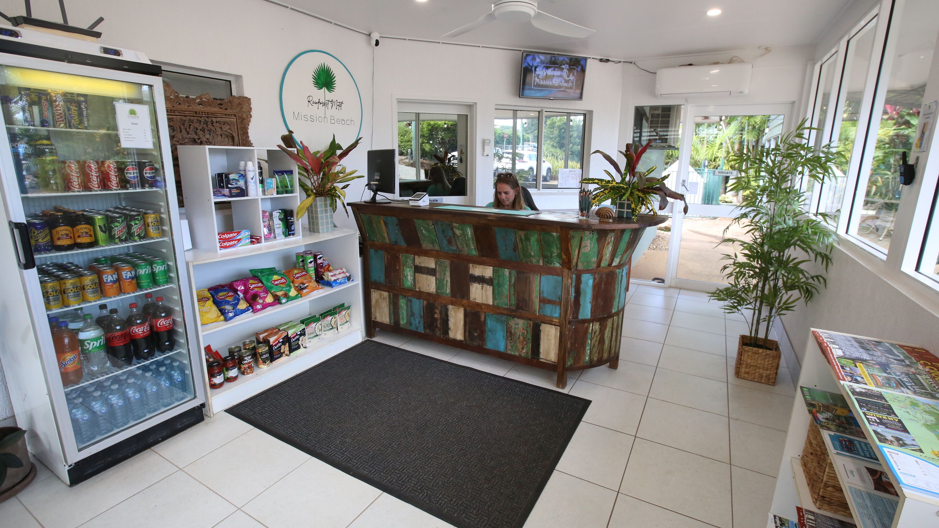 Un área de recepción con un refrigerador lleno de bebidas, un mostrador de madera y vistas al exterior.