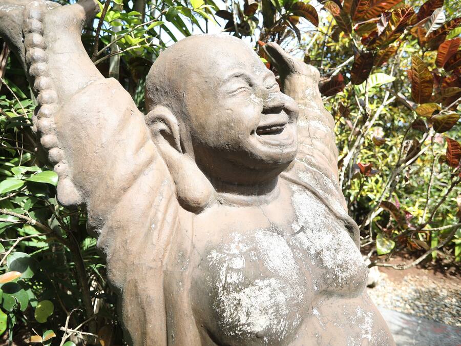 Una estatua de piedra de una figura con los brazos levantados, rodeada de follaje.