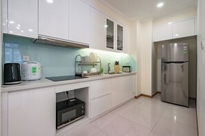 A modern kitchen with white cabinets, a stainless steel refrigerator, a built-in oven, and a coffee maker. - Chip Stay (Ho Chi Minh City)