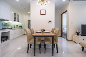 A modern kitchen with white cabinets, a microwave, and a dining area with a wooden table and four chairs. - Chip Stay (Ho Chi Minh City)