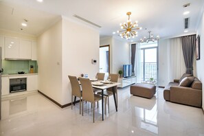 A modern living room with a sofa, a dining table with chairs, a kitchen area with cabinets, and a chandelier. - Chip Stay (HO CHI MINH)
