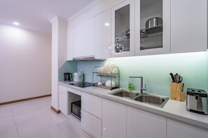 A modern kitchen with white cabinets, a stainless steel sink, a dish rack, a kettle, and a toaster. - Chip Stay (Ho Chi Minh City)