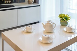 A white table with a teapot and two cups, a vase with yellow flowers, and a window in the background. - Chip Stay (Ho Chi Minh City)