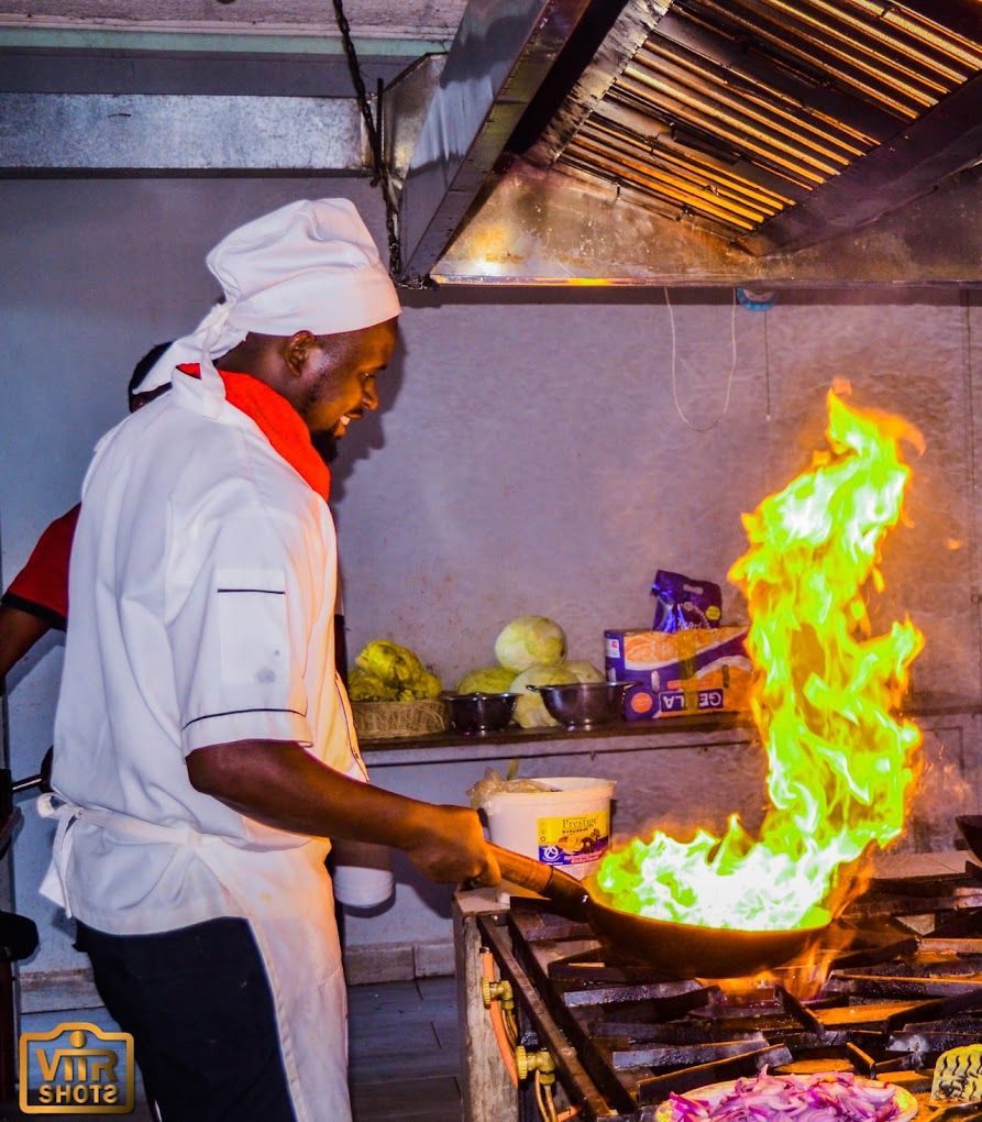 A chef performing a flambé with a pan on a stove in a kitchen.
