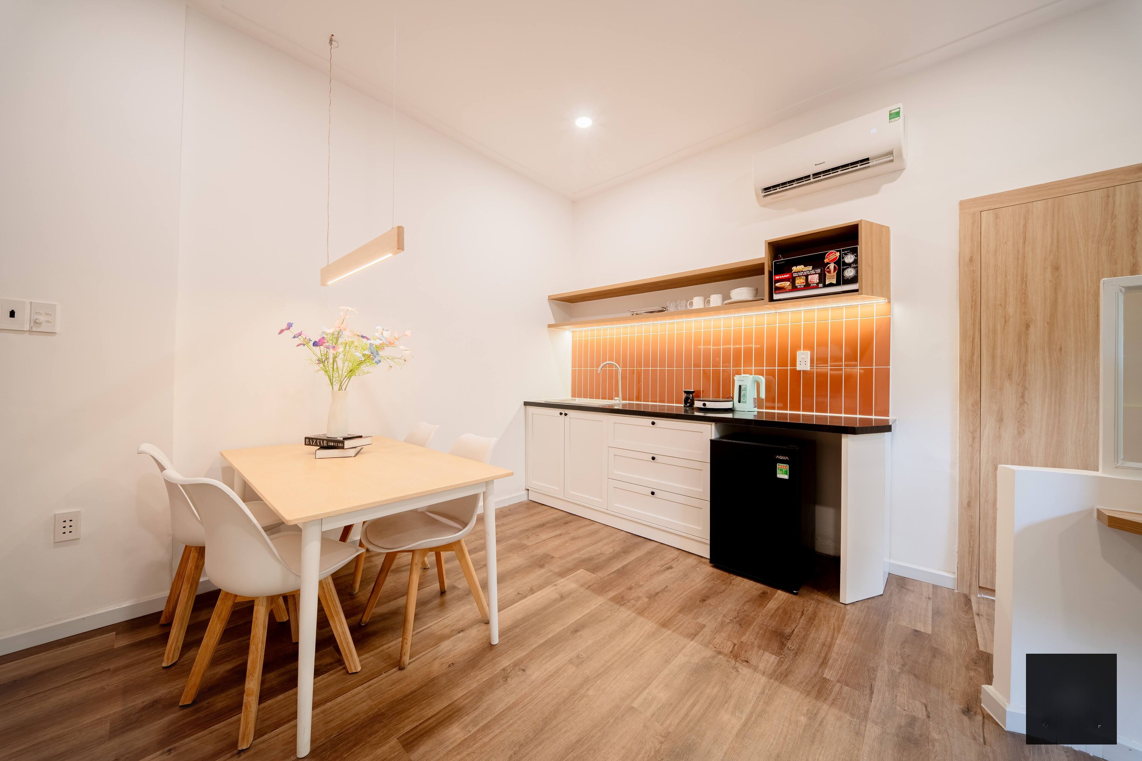 Una cocina moderna con armarios blancos, una encimera de madera y un horno empotrado. Hay una mesa de comedor con sillas y un jarrón con flores.