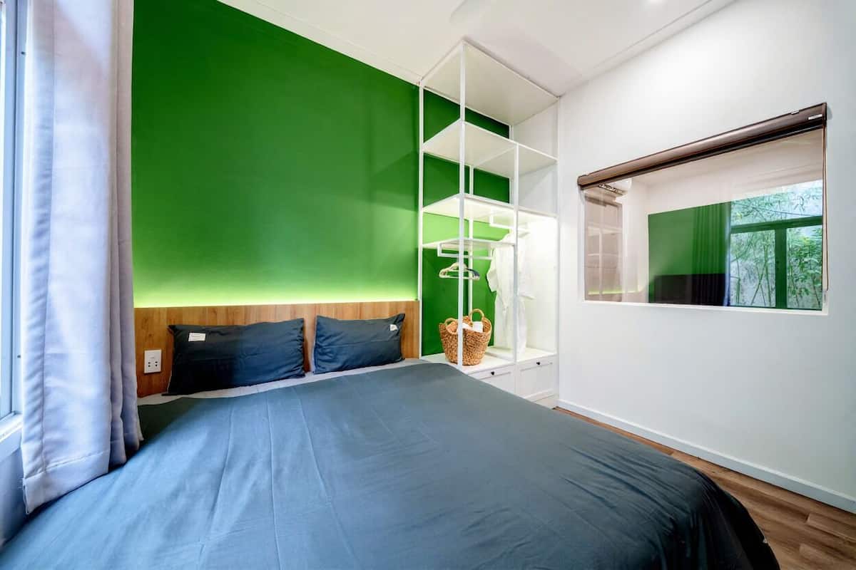 Un dormitorio moderno con una pared de acento verde, una cama grande, un estante blanco y una ventana con vistas a la vegetación.