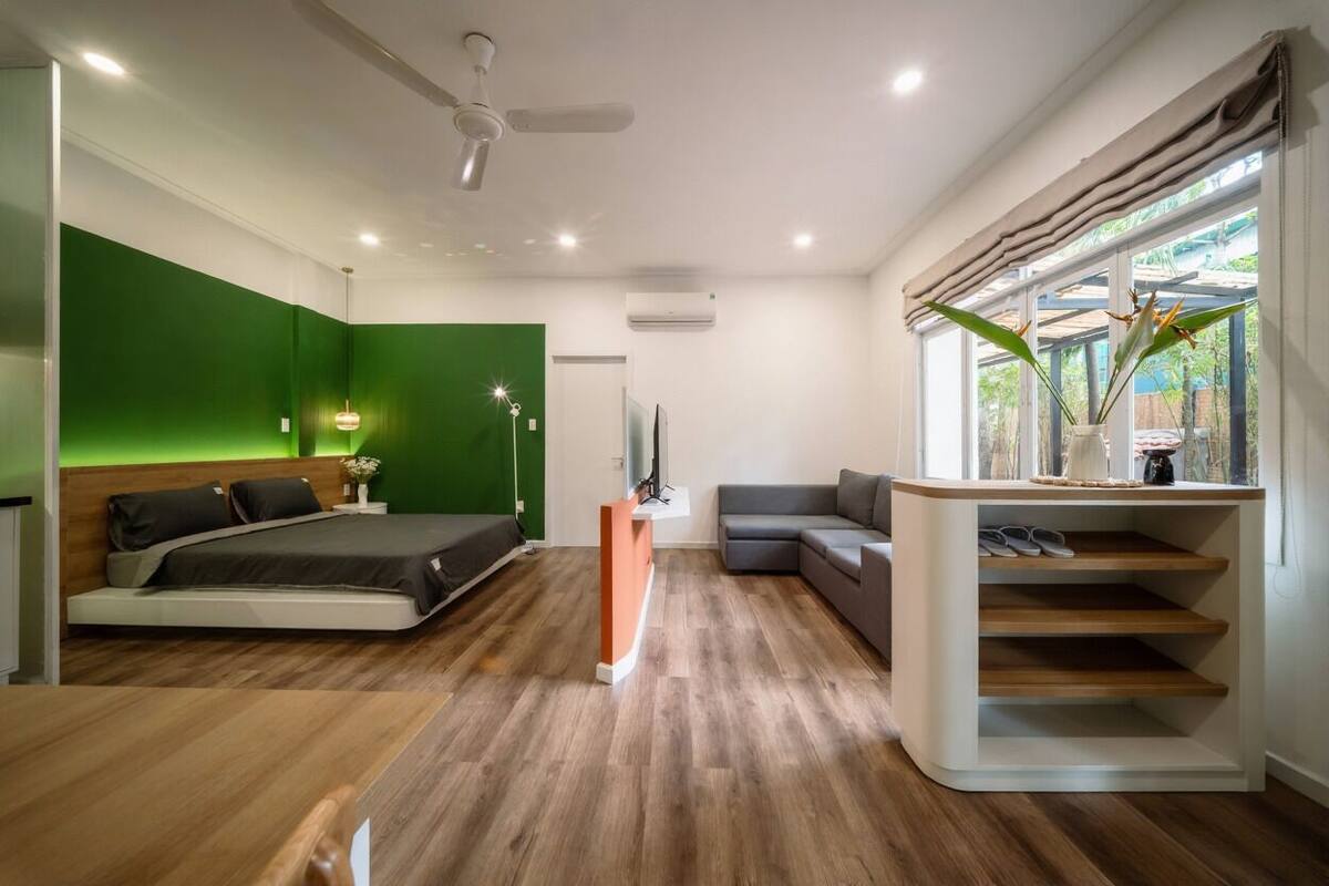 Un dormitorio moderno con una pared de acento verde, una cama con cabecera de madera, un sofá gris y un zapatero empotrado.