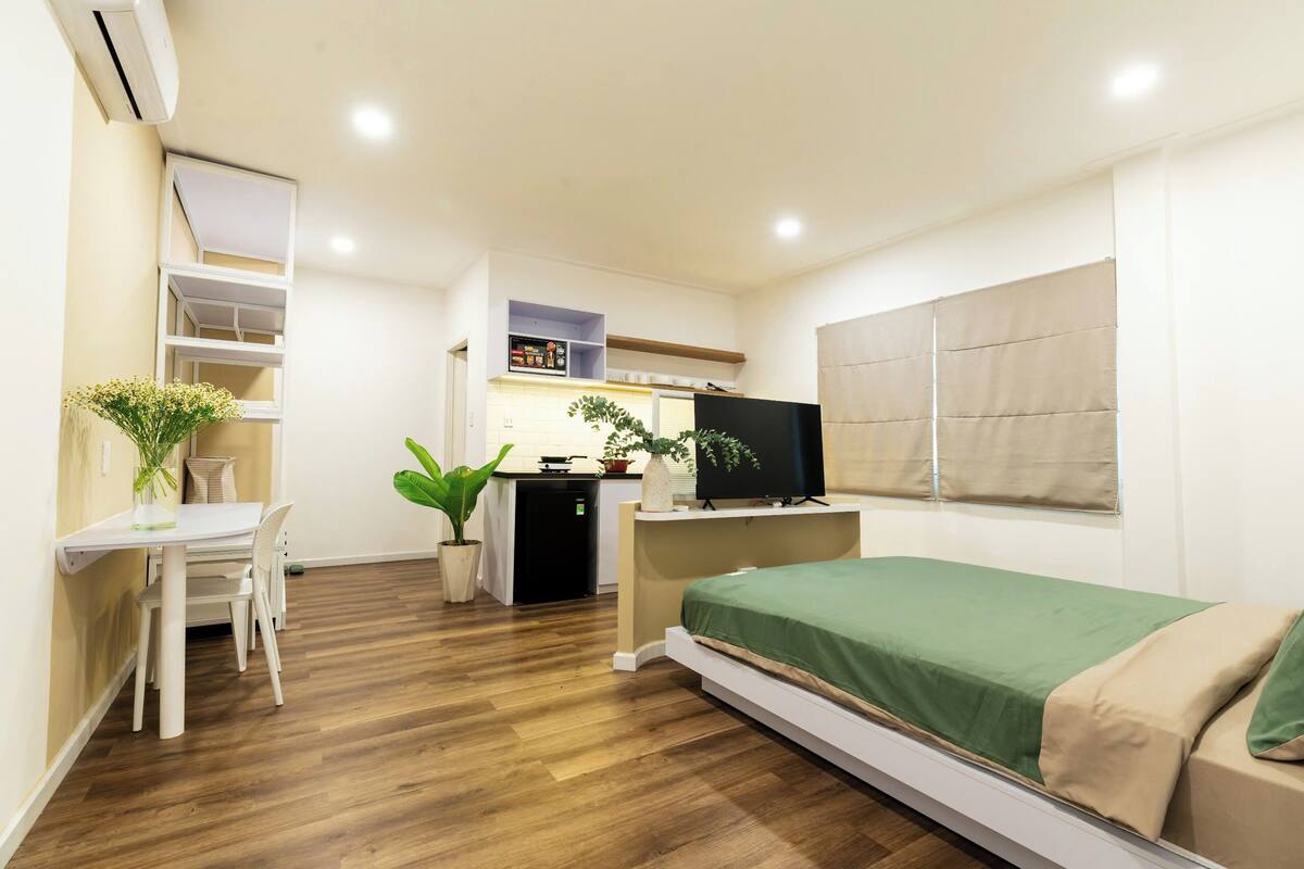 Una habitación funcional con cama, escritorio, televisor y kitchenette.