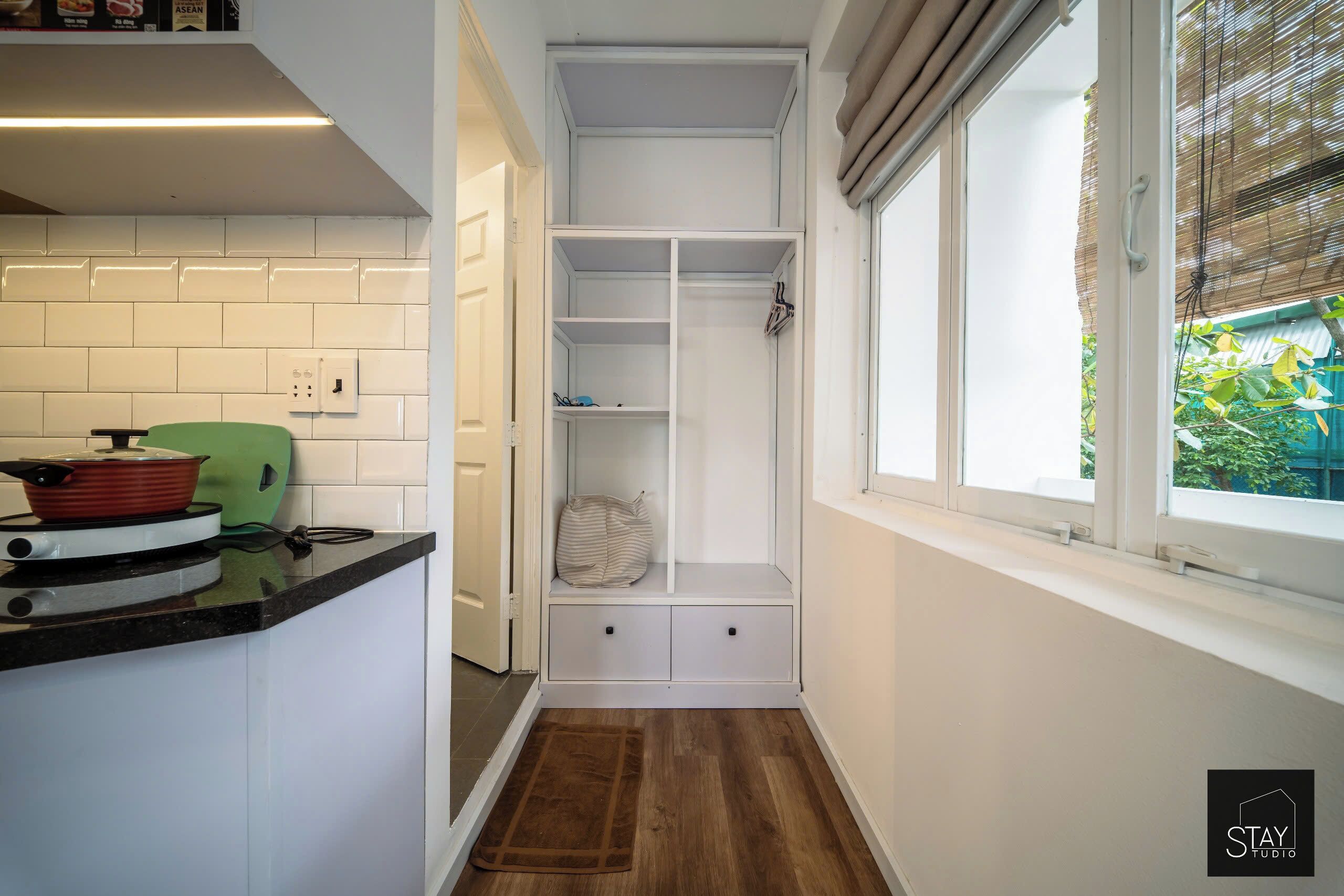 Una cocina compacta con armarios blancos, un electrodoméstico verde y una ventana con persianas.