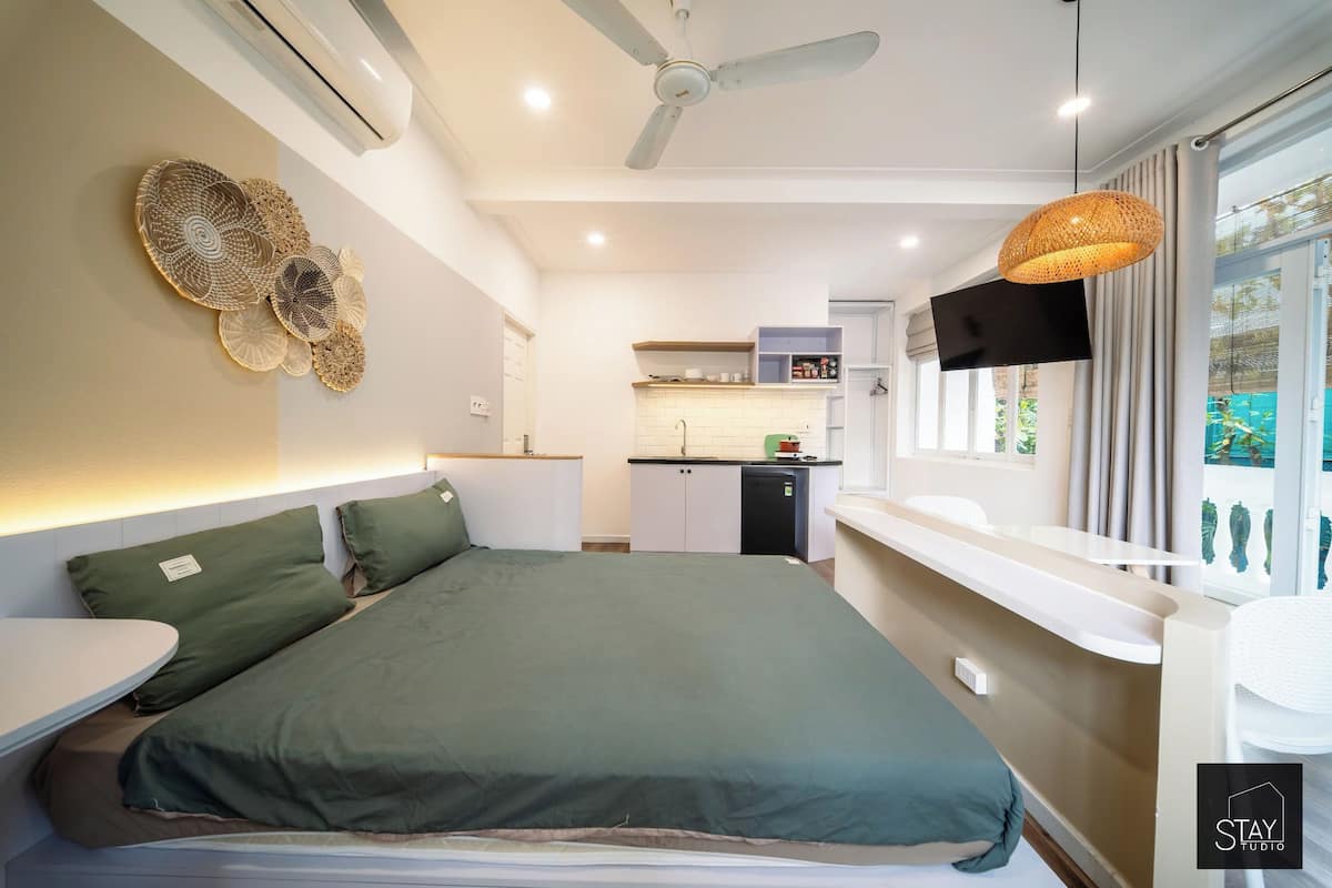 Un dormitorio moderno con una cama grande, una kitchenette pequeña y un televisor montado en la pared.