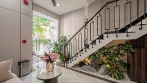 A modern lobby with a staircase, a round table with a vase of flowers, and a view of the outside. - Luxury Apartment Manhattan Grand Park By An Gia Hospitality (Ho Chi Minh City)