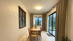 A dining area with a table and chairs, a window with curtains, and potted plants. - Nirvana Phangan Villas (Tambon Ko Pha-ngan)