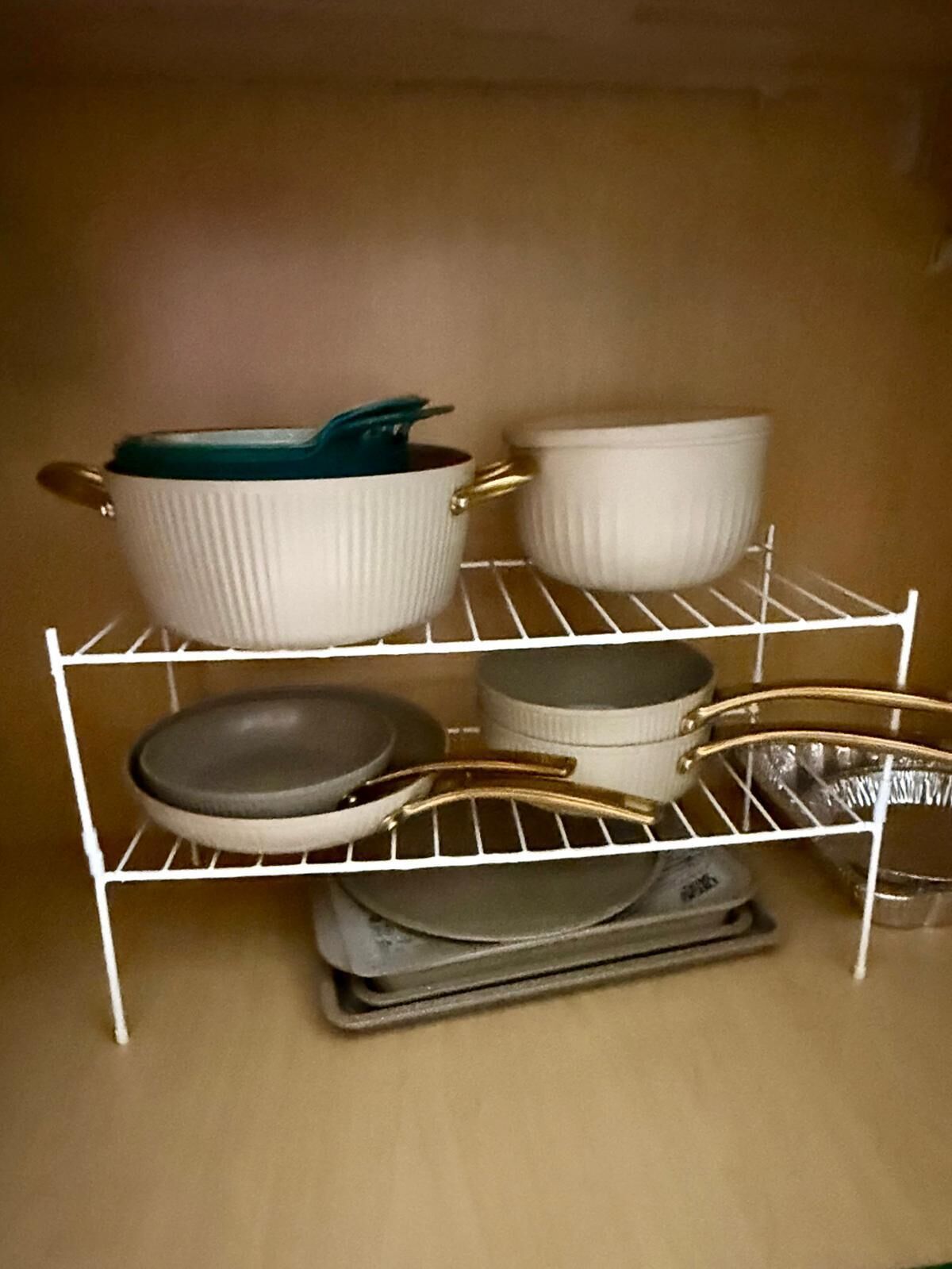 A white metal shelf unit with various kitchenware items including bowls, plates, and a pot.