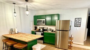Een moderne keuken met groene kasten, een roestvrijstalen koelkast, een houten kookeiland met krukken, en hanglampen.