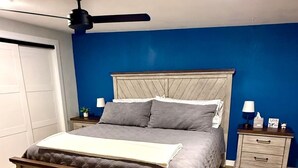Een slaapkamer met een bed, nachtkastje, plafondventilator en een kledingkast.