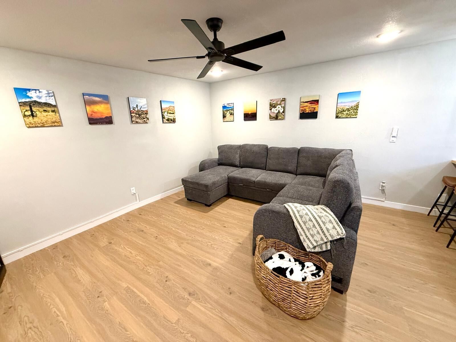 A living room with a sectional sofa, a ceiling fan, and a wall with framed landscape paintings.