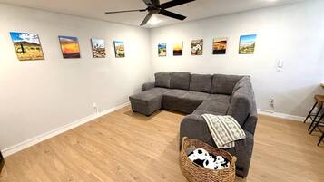 A living room with a sectional sofa, a ceiling fan, and a wall with framed landscape paintings.