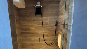 Un baño pequeño y moderno con piso de madera, inodoro, ducha con puerta de vidrio y grifo empotrado en la pared.