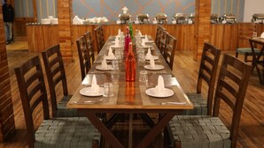 Une longue table à manger, entourée de chaises, avec une bouteille et des verres, dans un restaurant aux murs en bois et dont l’un des murs est décoré de motifs géométriques.