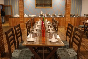 Uma longa mesa de jantar posta com cadeiras, uma garrafa e copos em um restaurante com paredes de madeira e um design geométrico.