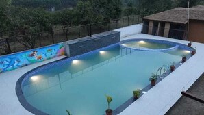 Une piscine ornée d’une fresque murale, entourée de plantes en pot, et une structure à toit de chaume en arrière-plan.
