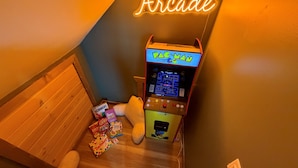 Une pièce avec une borne d’arcade Pac-Man, un jouet en peluche et des jeux de société.