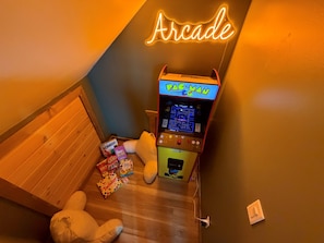 Ein Zimmer mit einem Pac-Man-Spielautomaten, einem Stofftier und Gesellschaftsspielen.